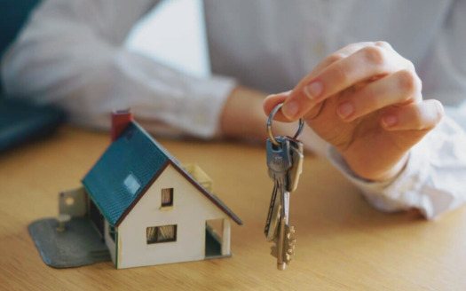 Mujer sosteniendo unas llaves con una maqueta de una casita a su derecha.