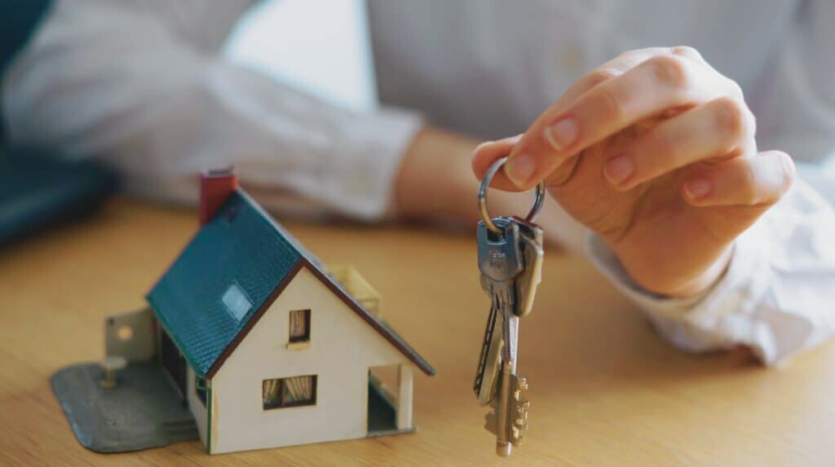 Mujer sosteniendo unas llaves con una maqueta de una casita a su derecha.